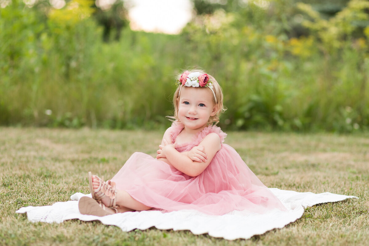 Little girl sitting on a blanket on the grass smiling at the camera