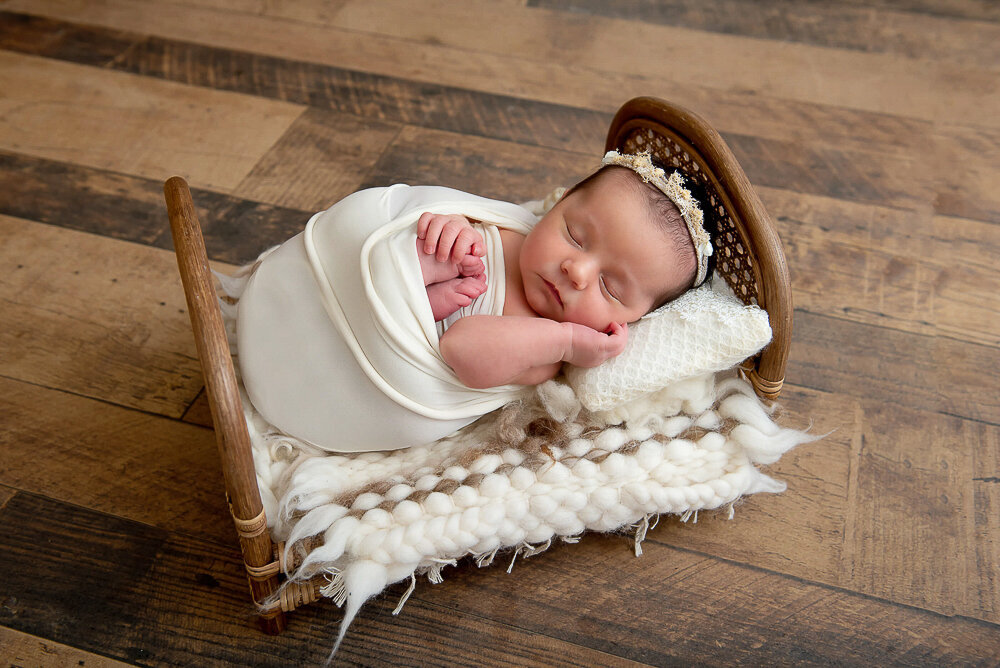 newborn girl wrapped in cream on a tiny bed.