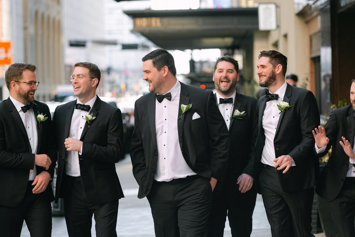 groom and groomsmen walking outside the entrance of The Adolphus in Dallas, captured in a stylish and relaxed wedding portrait.