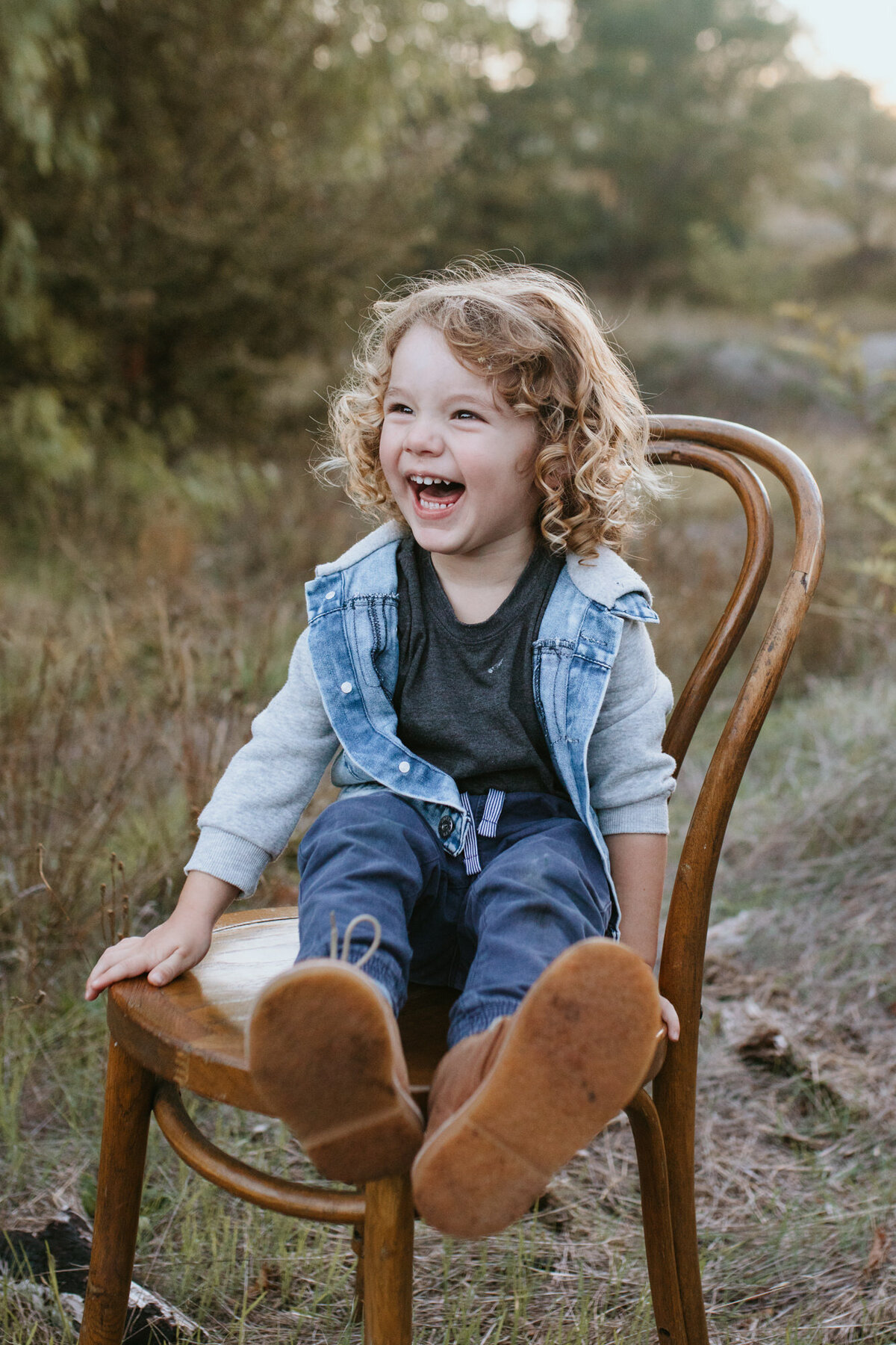 An emotionally-filled moment of a brown haired boy laughing while sitting on a chair in a grass field in Bendigo. 