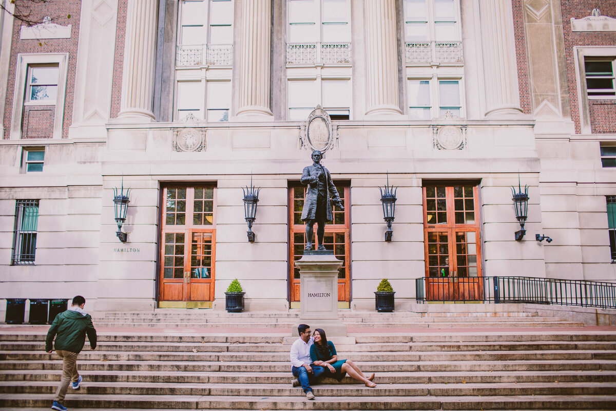A couple sitting on the steps in front of a statue and building at columbia university in nyc