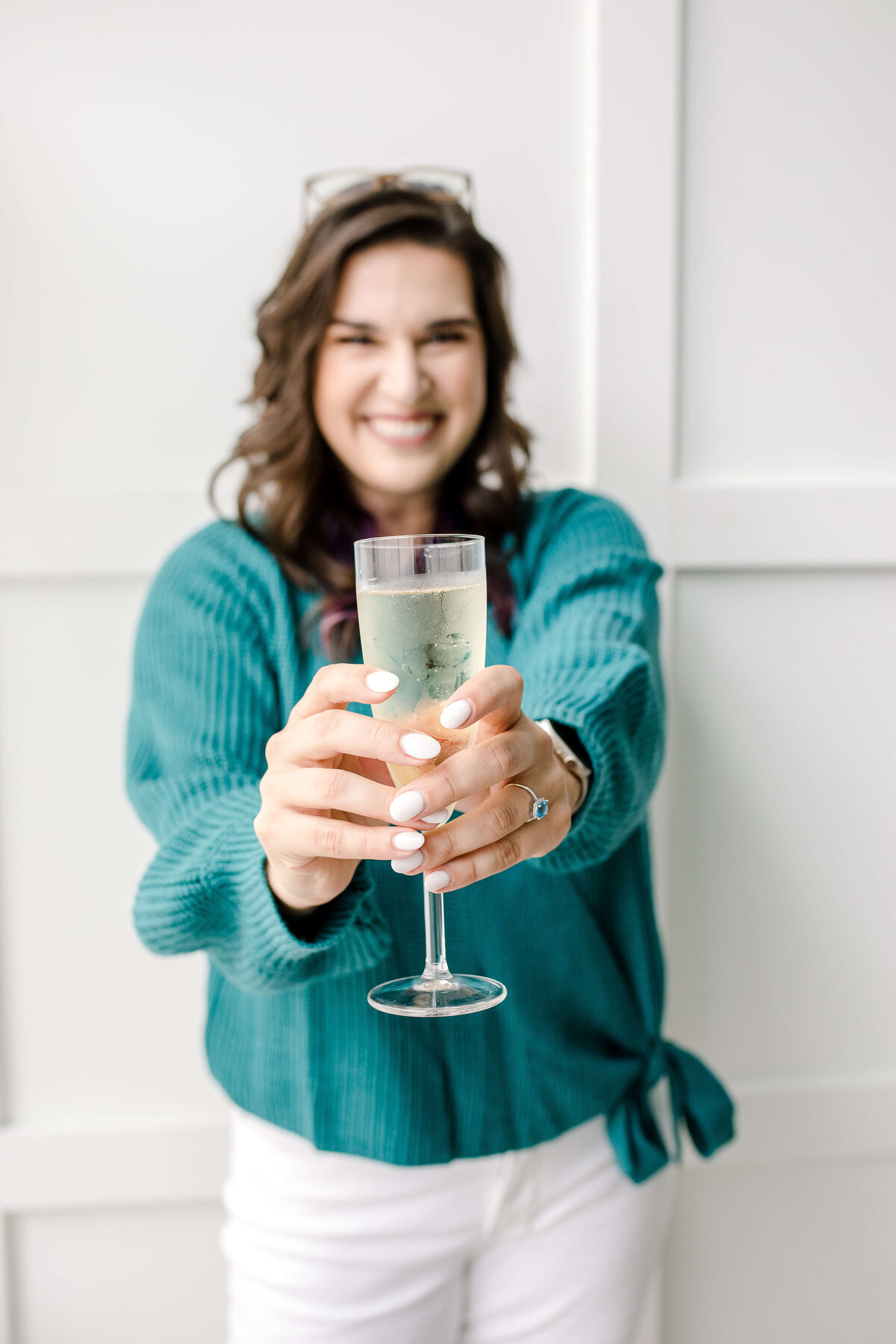 brand photo with woman holding a glass of champagne towards the camera as she smiles for her brand photography