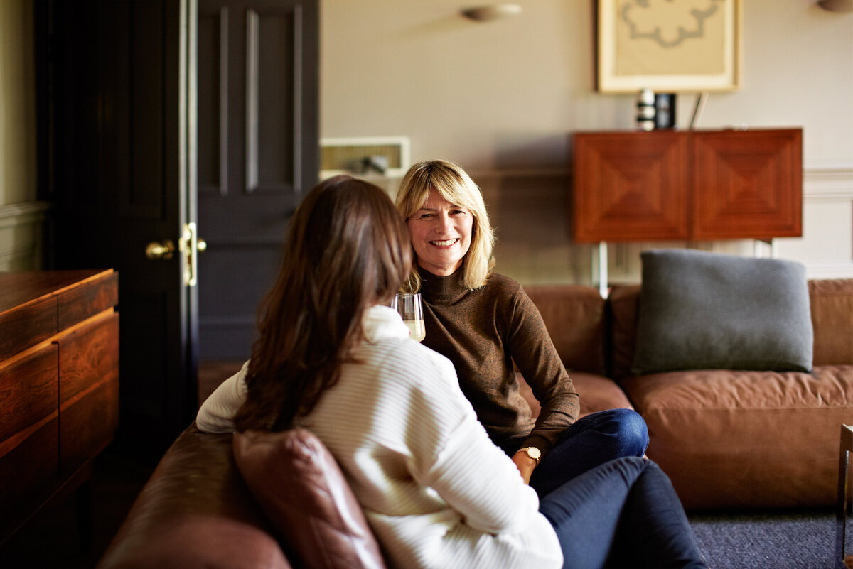 Two women sitting on a couch talking and smiling