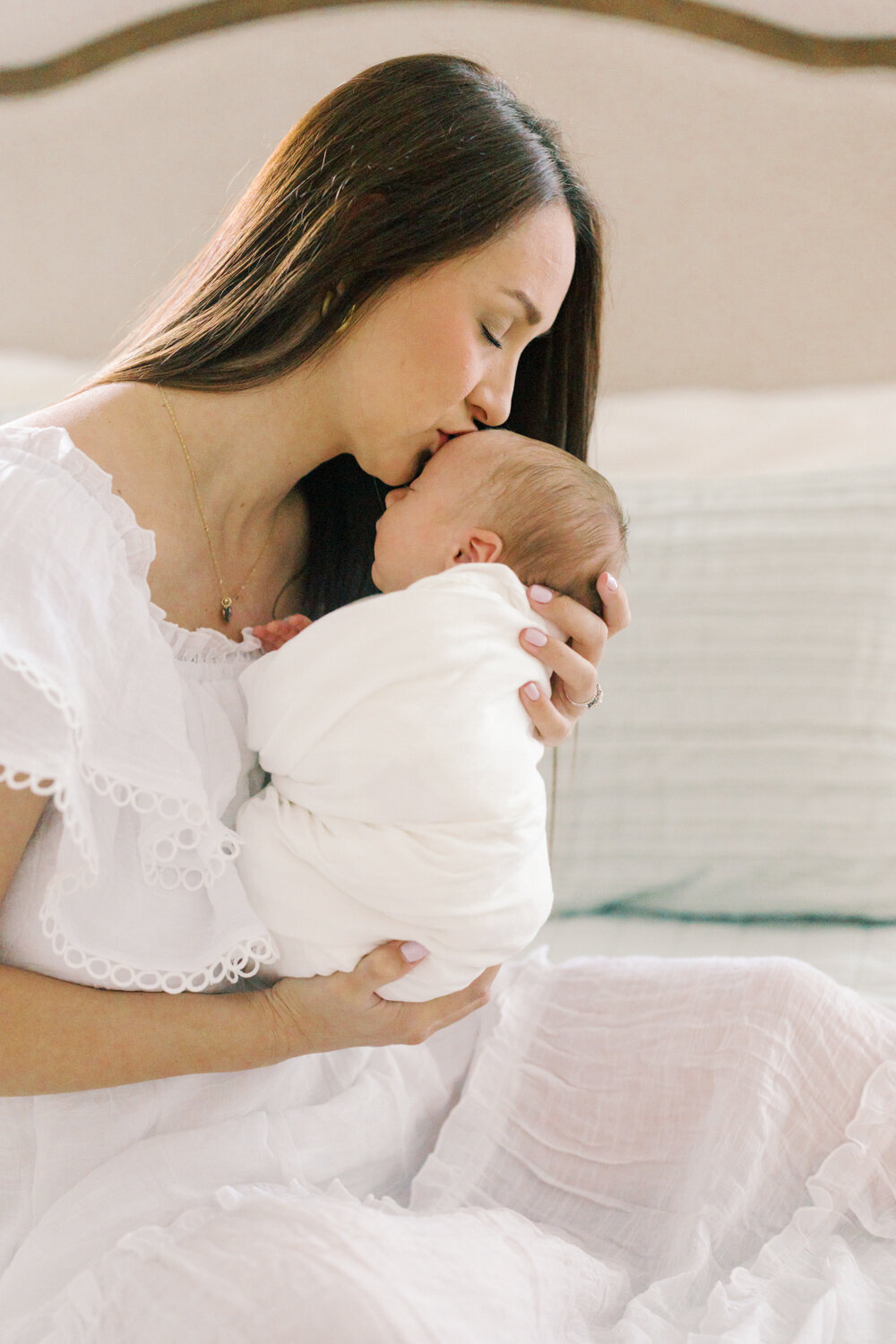 mom-holding-newborn-son-on-bed-kissing-his-forehead