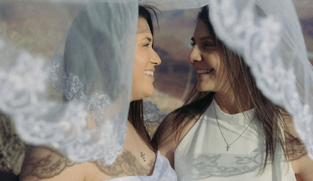 A couple with a veil over them smiling at each other.