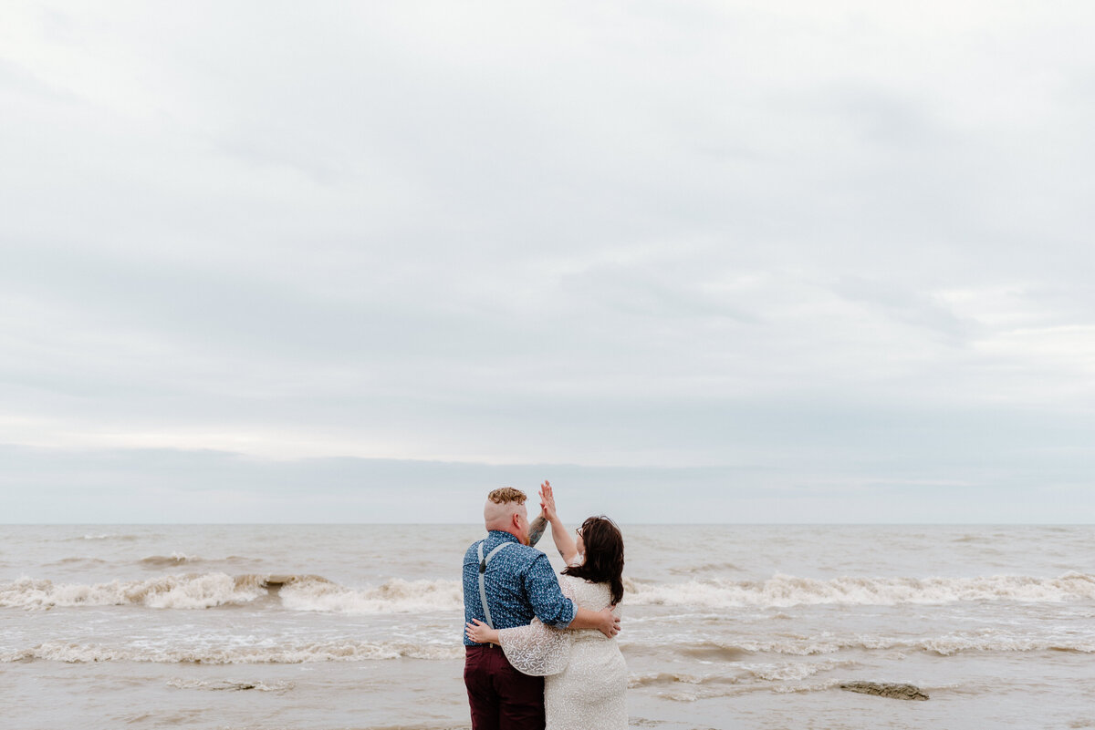 lake erie elopement bride and groom high-five on the shore of lake erie