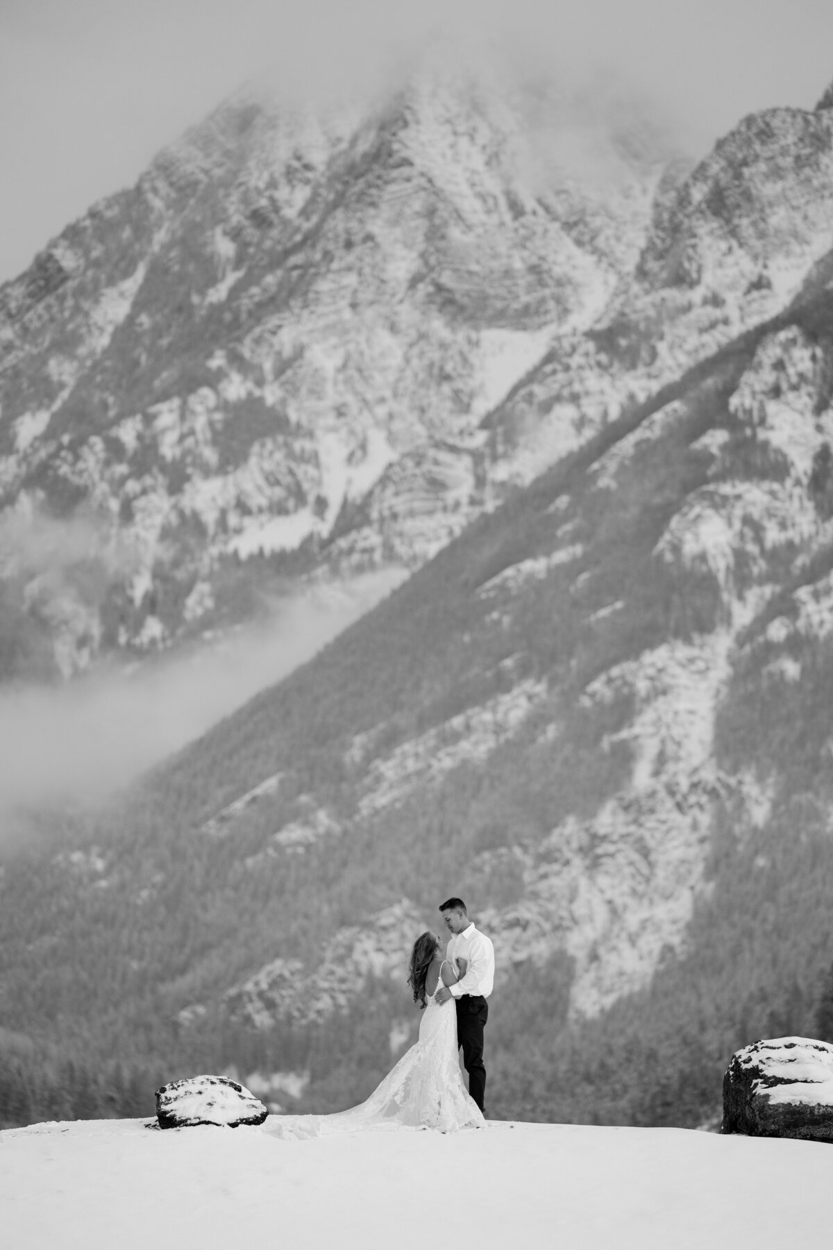 black and white image bride and groom kissing  by mountain