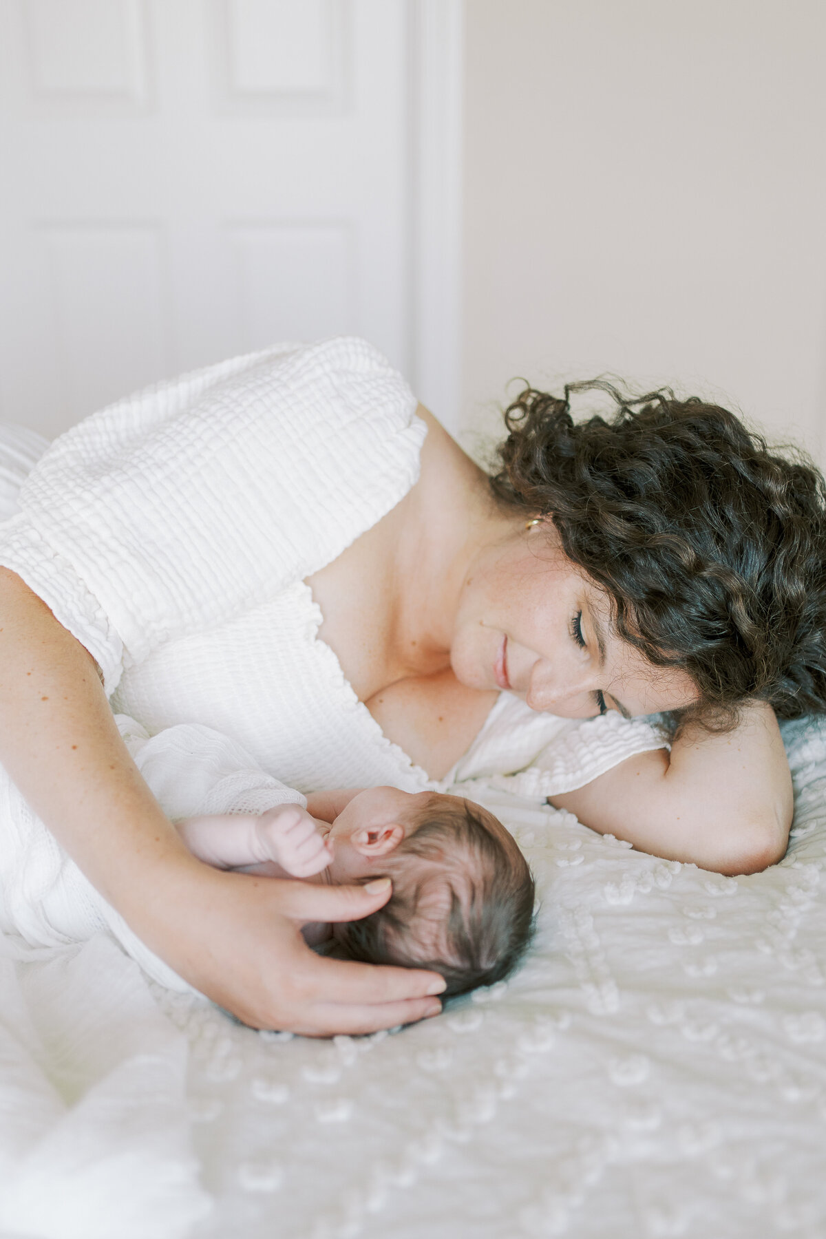 mom laying on bed smiling at newborn baby