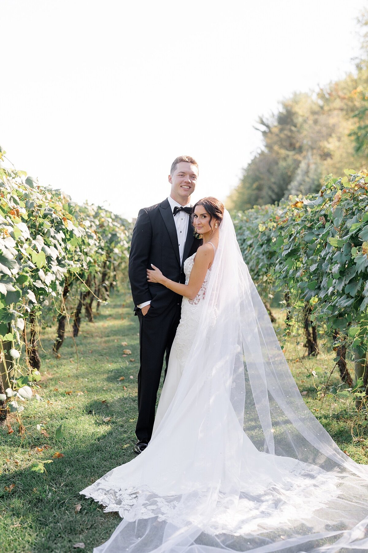 Columbus wedding  photographer  captures vineyard wedding photos with bride and groom standing in between rows of vines and the bride embracing the groom while they both smile