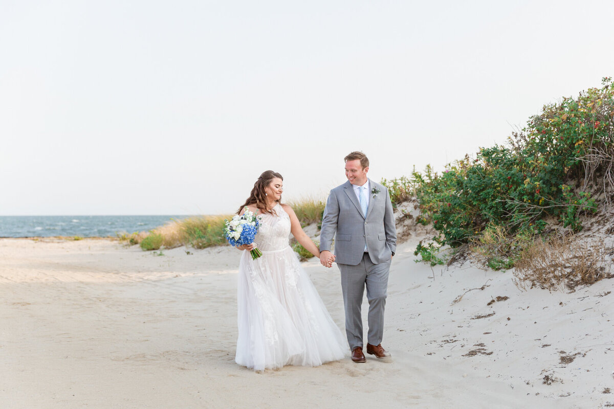 A couple walks hand in hand on the beach on theor wedding day