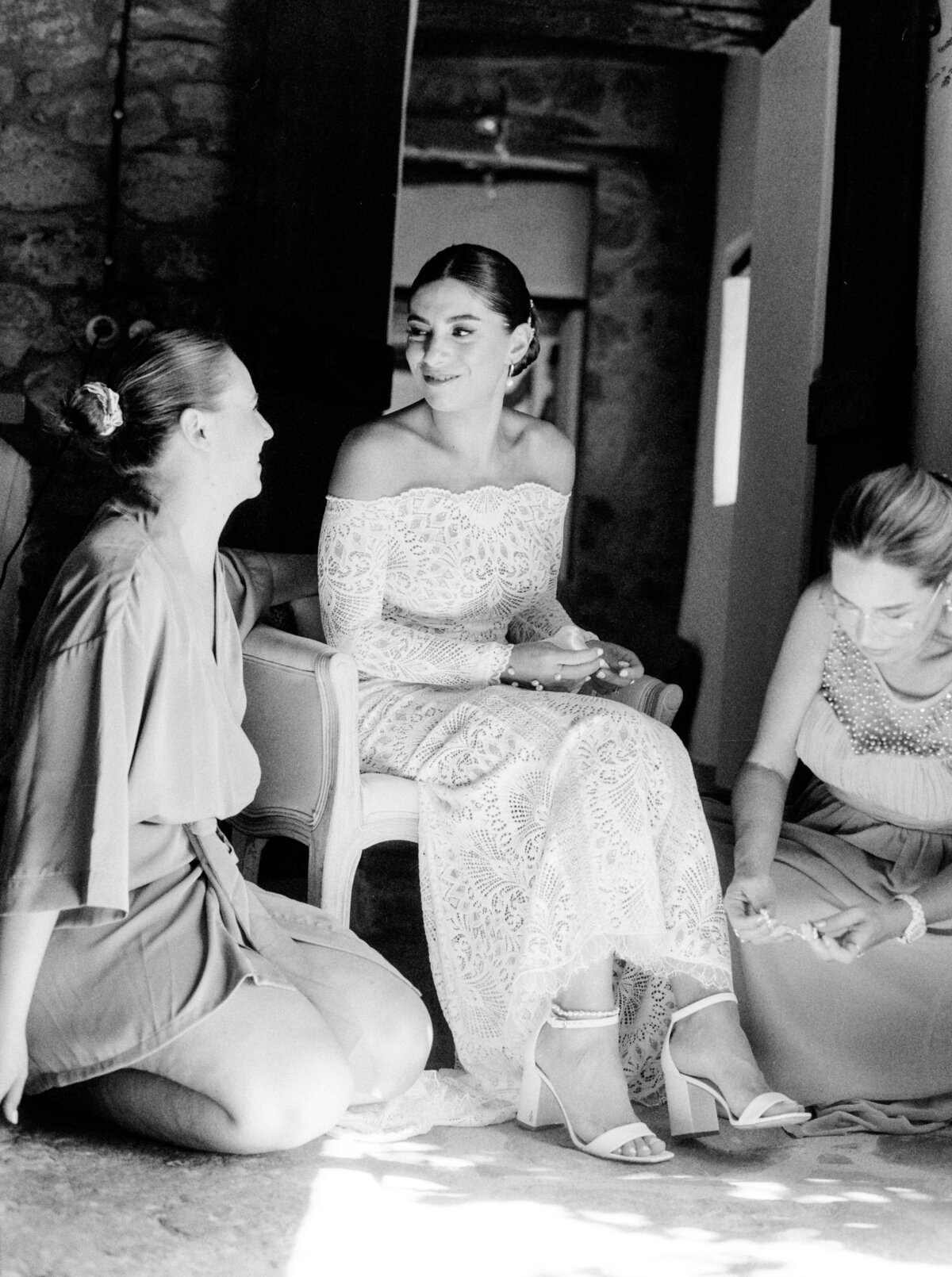 Black and white film photograph of bride in all lace wedding gown with maid of honor and mother while getting ready photographed by Italy wedding photographer at Villa Montanare Tuscany wedding