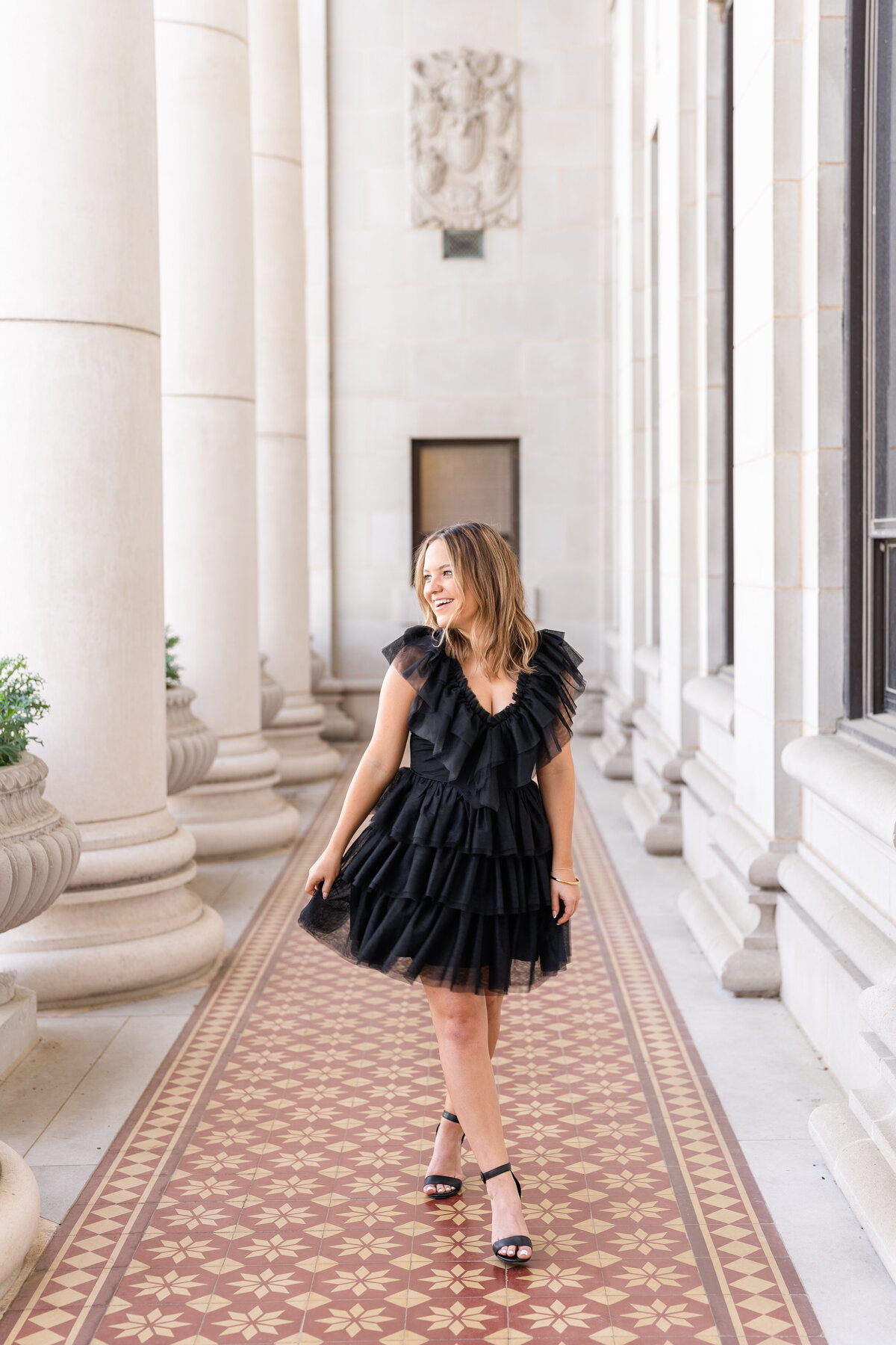 Texas A&M senior girl swishing dress and laughing over shoulder while walking in fluffy black dress in columns of Administration Building