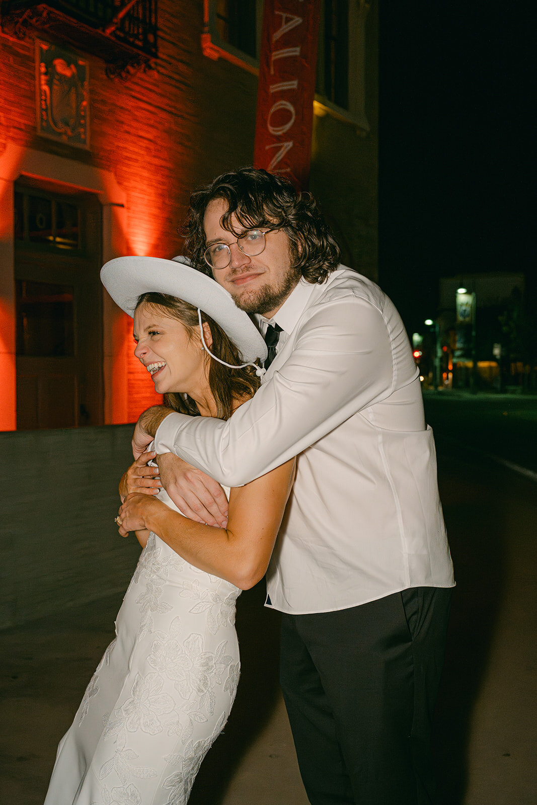Bride in groom’s arms, both smiling, at end of reception outside The Battalion