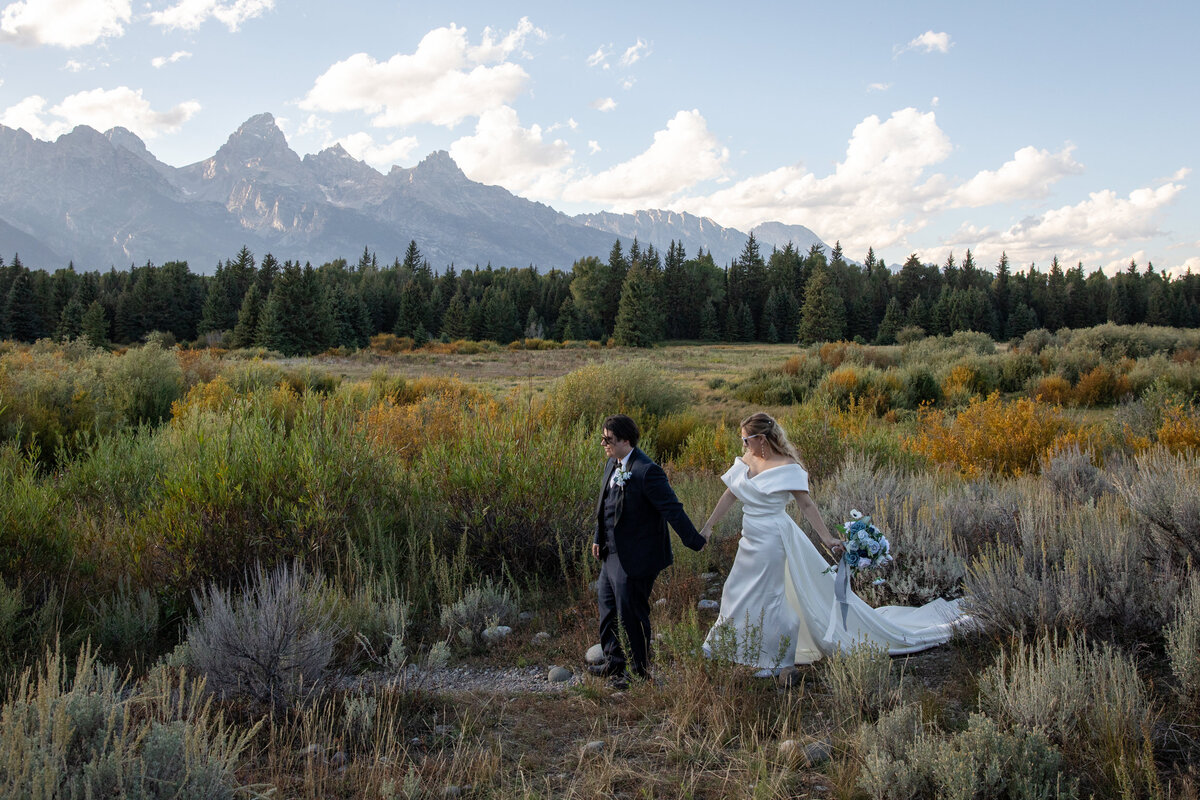 A bride and groom walk hand in hand through a field on their Wyoming elopement day.