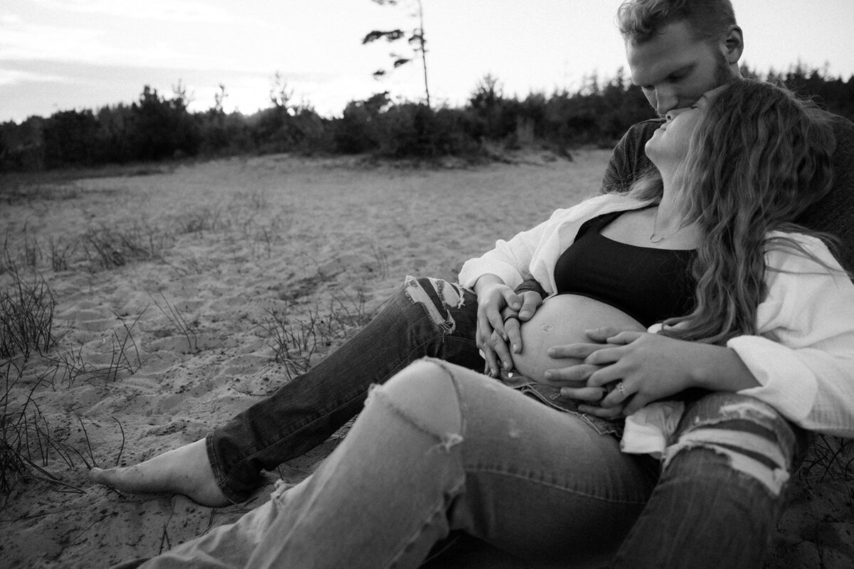 Woman looks up at man as he holds her and they enjoy each other on the beach in Oregon. 