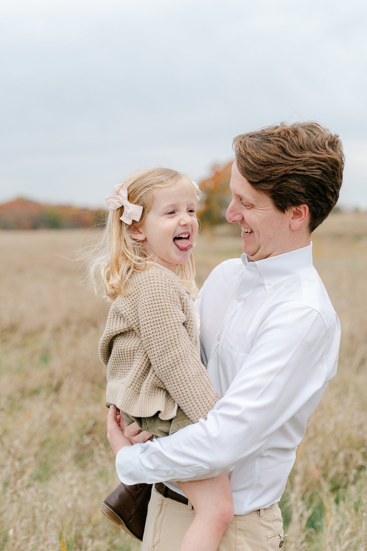 Dad laughs at his daughter making a silly face while he holds her