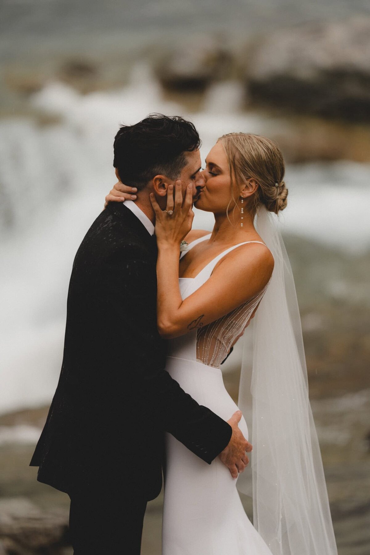 Wedding couple kissing and holding each other in front of waterfall