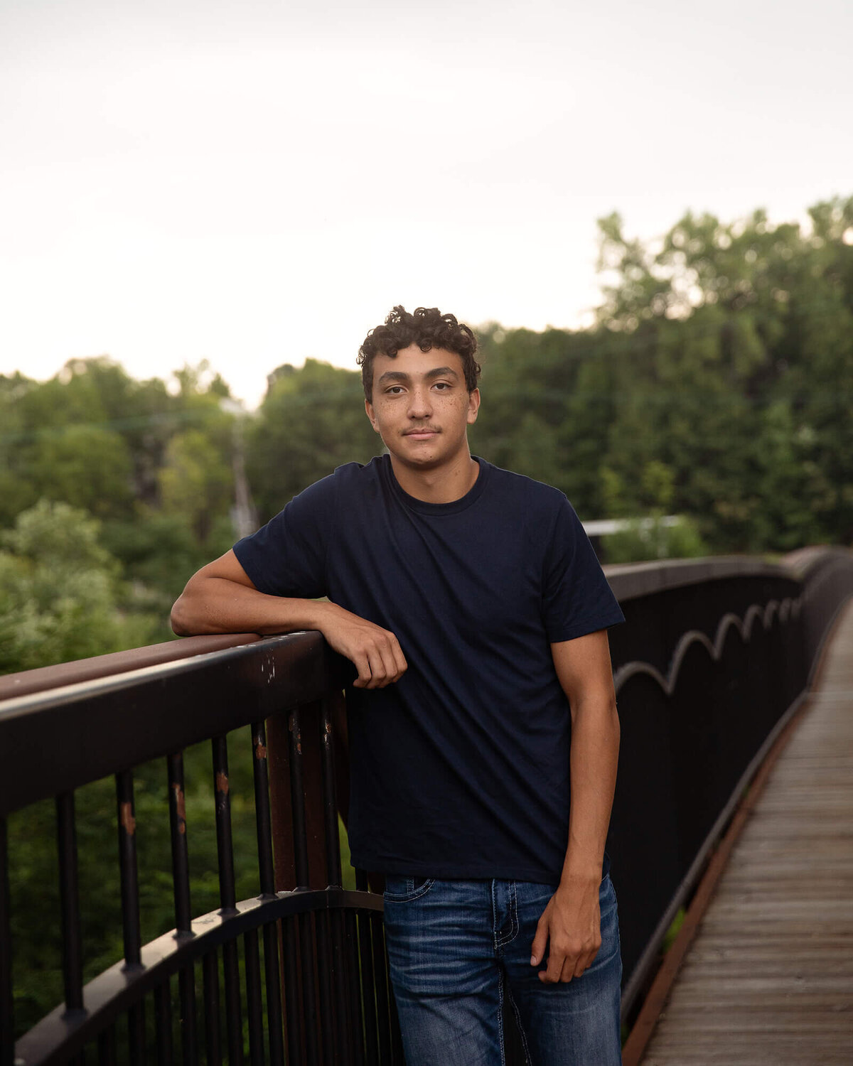 Senior boy leaning his arm on the railing of a bridge.