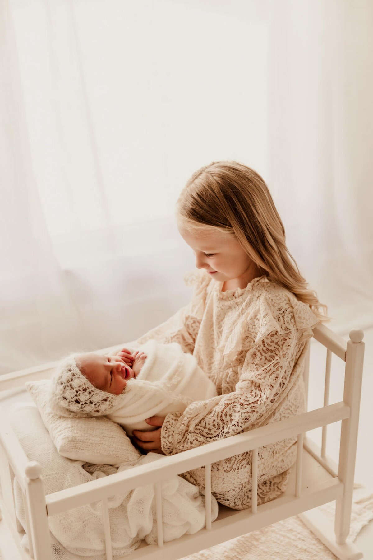 Girl with blonde hair looking down at her newborn baby sister, Yukon, Oklahoma.