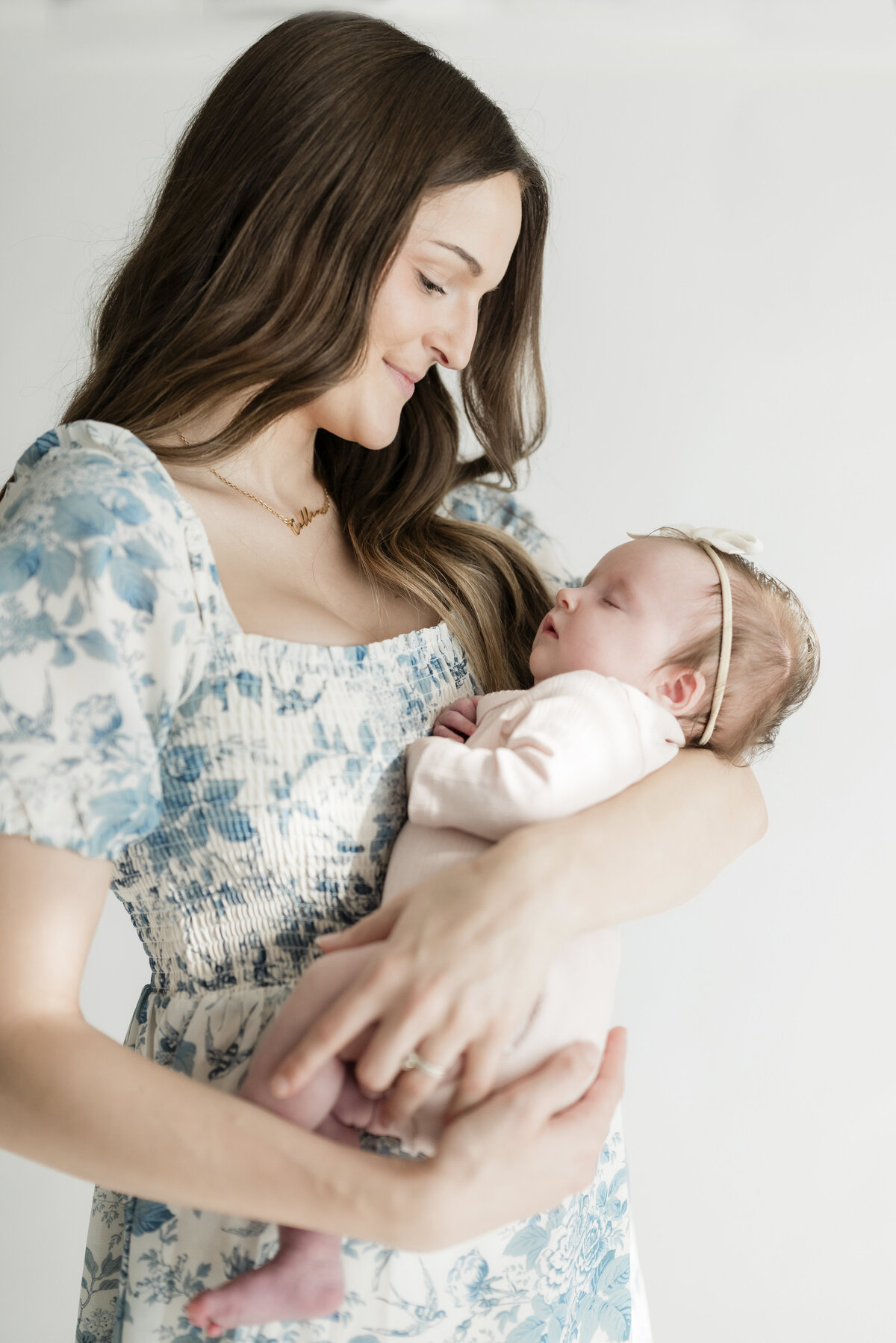 Mom holding her baby against her chest while smiling gently, framed in soft window light.