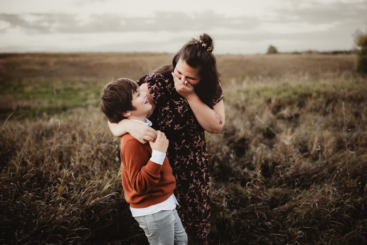 mom and son giggling as she has an arm around him for a hug