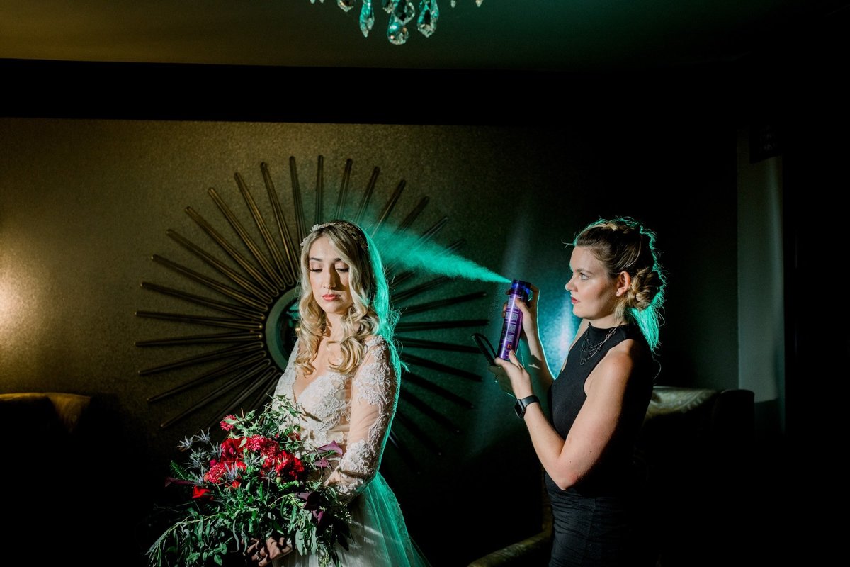 Bridesmaid sprays hairspray to the back of the Bride's hair as it gives off a green mist