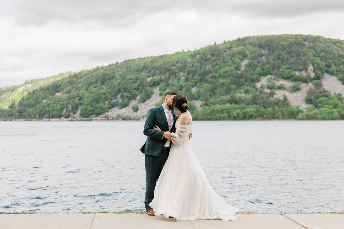 bride and groom kissing in front of a lake