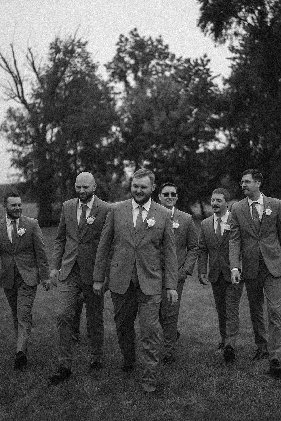 Black and white candid of the groomsmen walking together during wedding party portraits at The Blue Heron Barn.