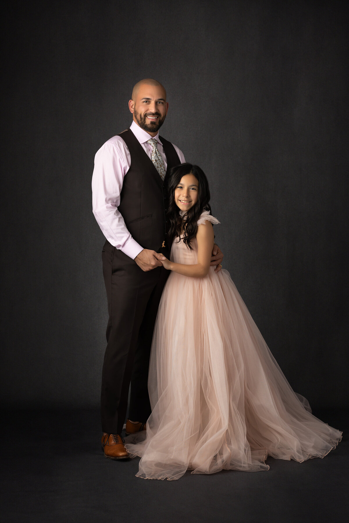 A Dallas family photographer captures a heartwarming moment of a father and daughter smiling together, with the daughter in a soft pink gown and her father in a suit.