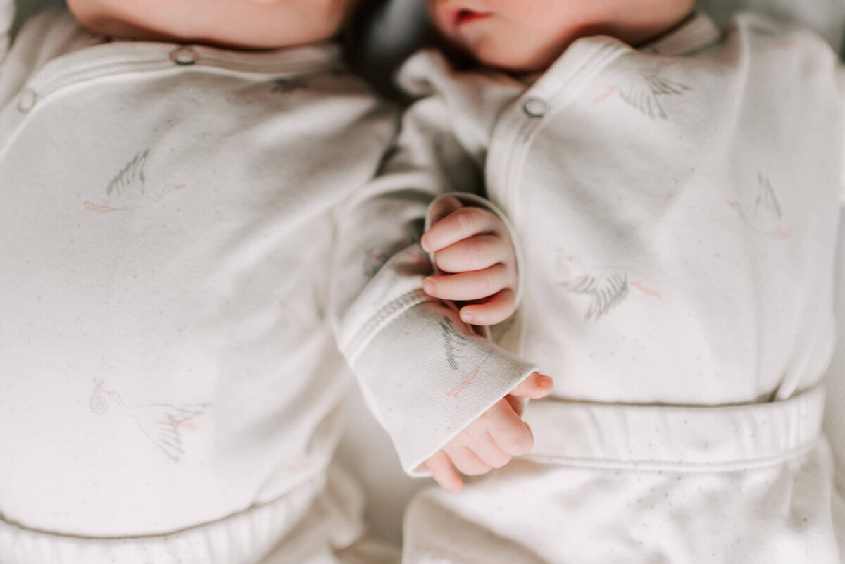 newborn boy twins holding hands while sleeping together