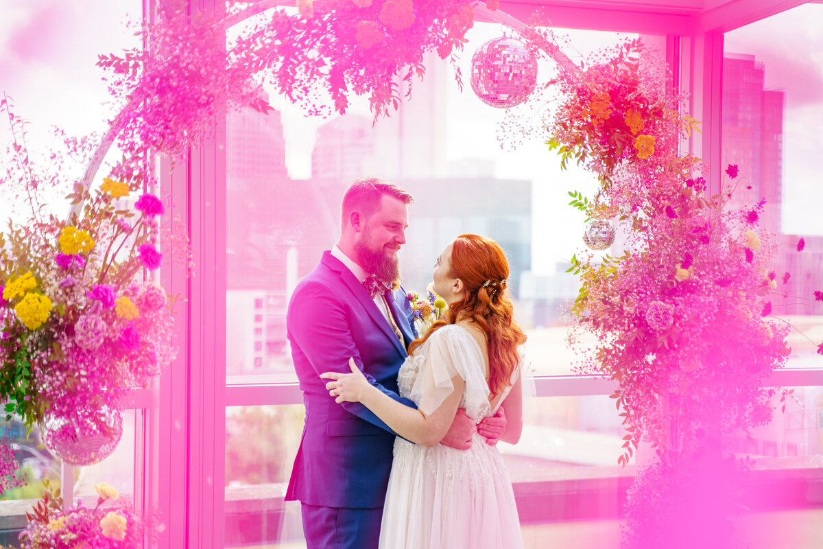 Bride and groom look lovingly at each other as they stand under their colorful floral arch at North 4th Corridor (The Revery) in Columbus, Ohio.