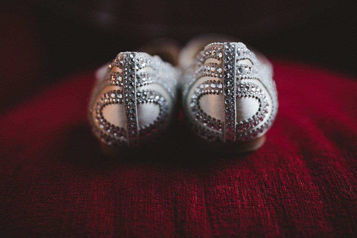 Silver art nouveau wedding shoes sitting on a dark red velvet cushion.