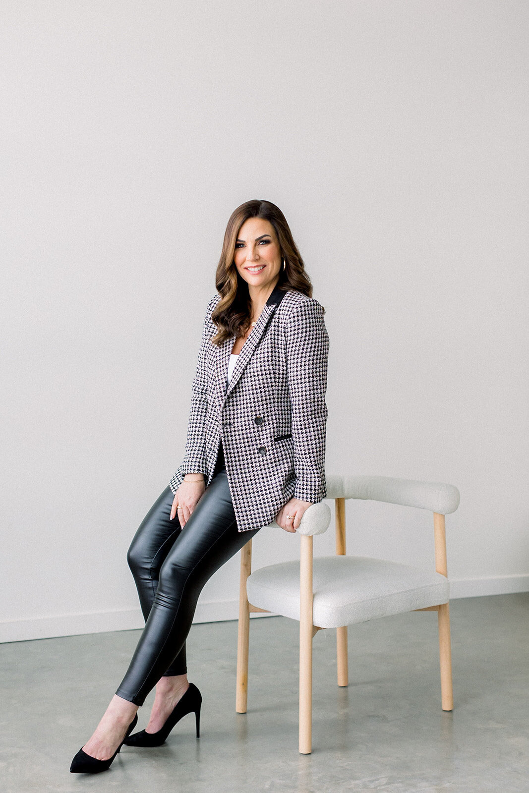 Brand photo of Calgary business woman in black and white checked blazer leaning against a white chair.