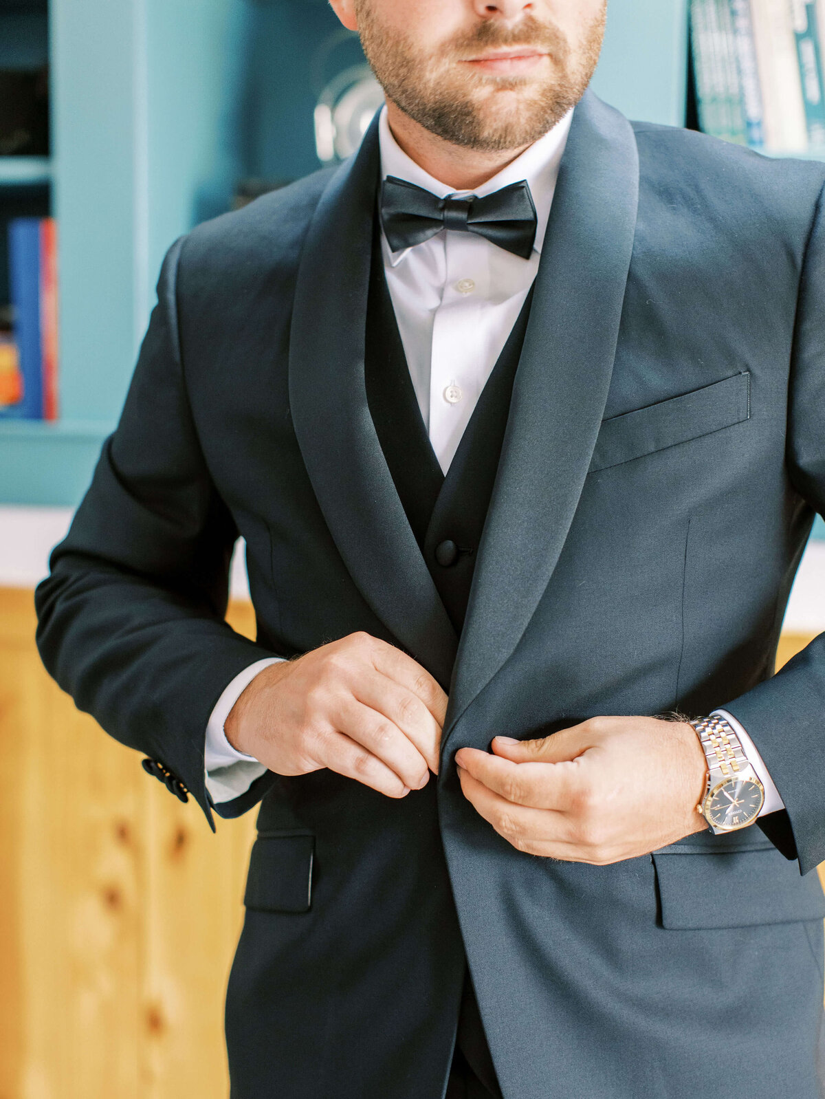 A close up of a groom buttoning up the buttons on his suit jacket before his luxury outdoor wedding.