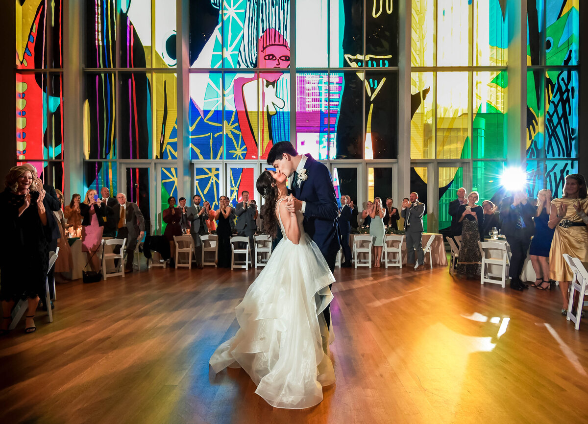 Bride-and-groom-kissing-on-dance-floor-of-the-Mint-Museum-Uptown-in-front-of-stained-glass-art-installation