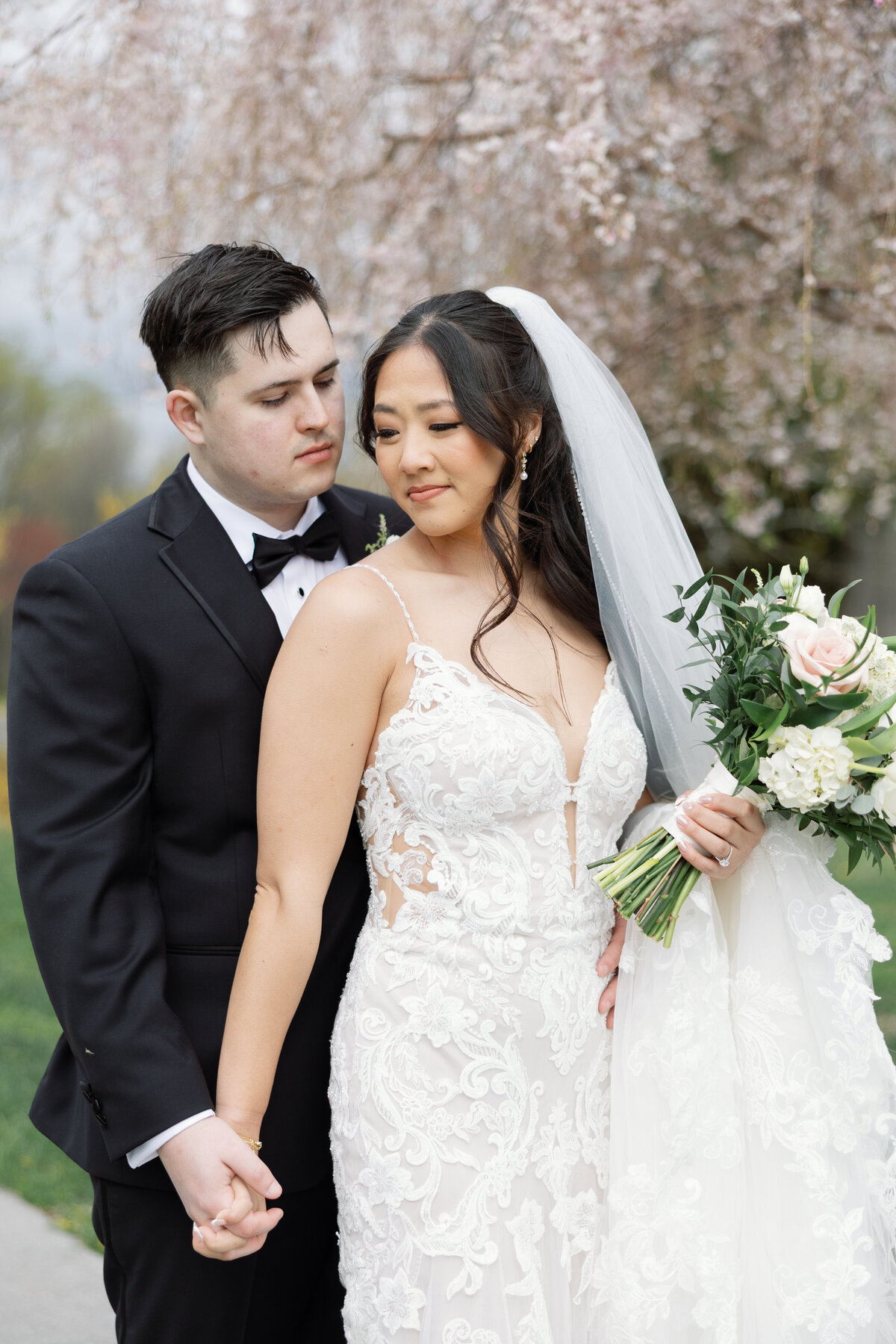 Couple holding hands beneath cherry blossom tree during spring wedding at Springfield Manor in Maryland.