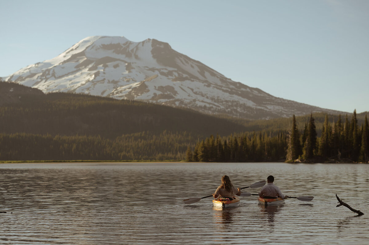 bride and groom kayak off into the sunset towards Mt. Bachelor after their private elopement ceremony