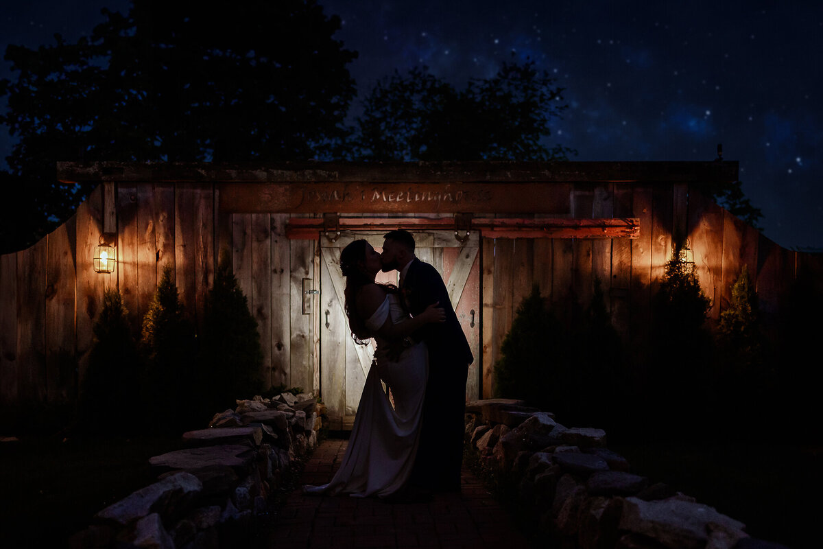 groom kissing bride in front of barn doors at josiah's meetinghouse barn doors in Epping NH