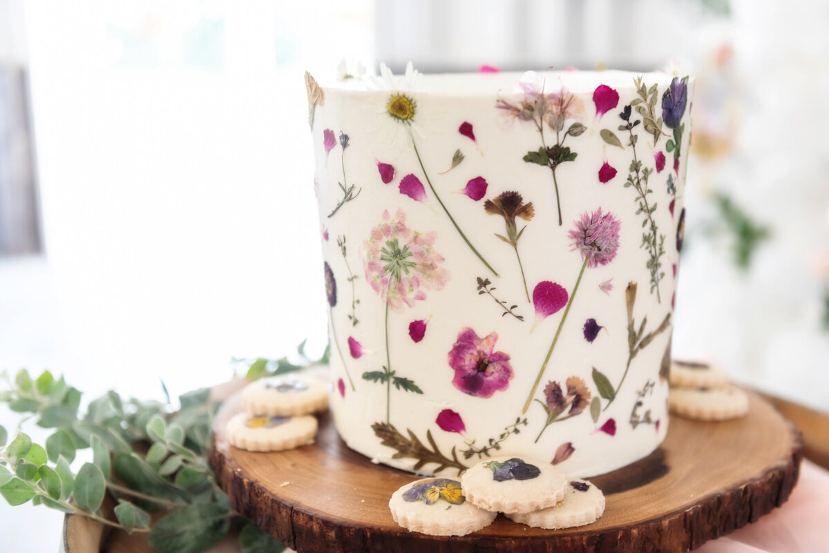 Simple professional single-tiered white wedding cake, decorated with pink and purple pressed edible florals, created by Black Dog Bakery, creative & eclectic cakes & desserts in Calgary, Alberta, featured on the Brontë Bride Vendor Guide.
