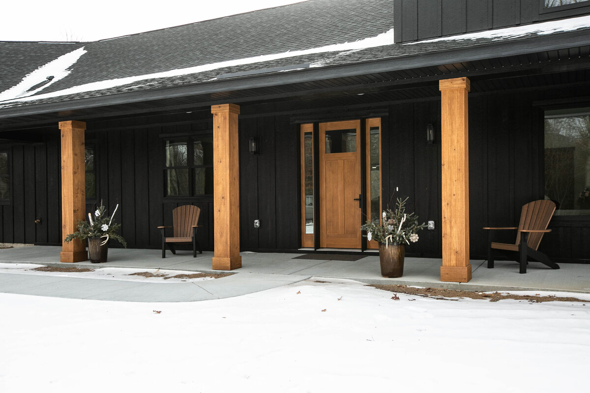 Exterior view of custom home in Elk River, Minnesota with black siding, wood details and front porch built by Cornerstone Custom Builds