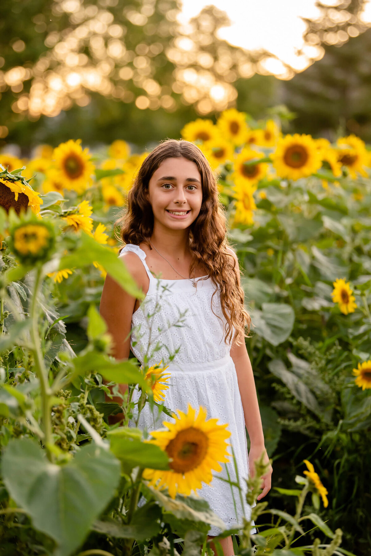 Teenage girl wearing white standing in a sunflower field for her summer family photos