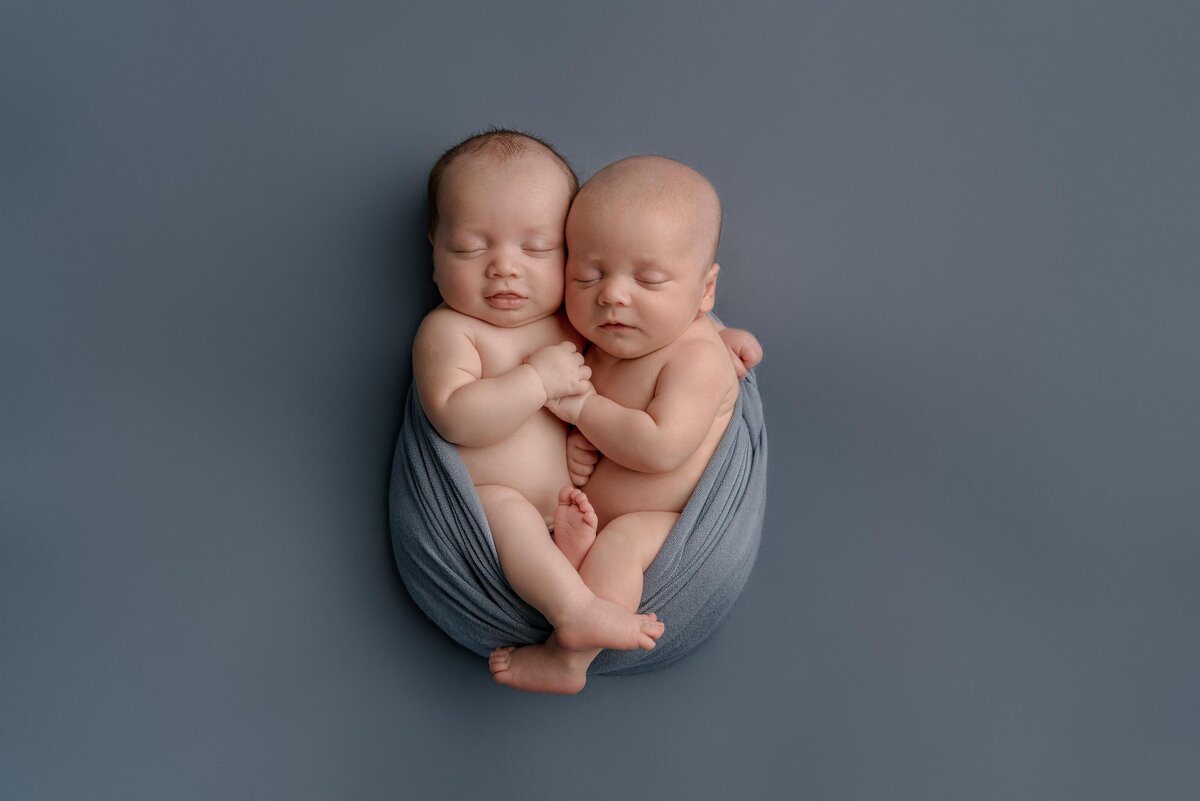 Navarre FL newborn photographer twin studio session wrapped together in blue swaddle blanket.