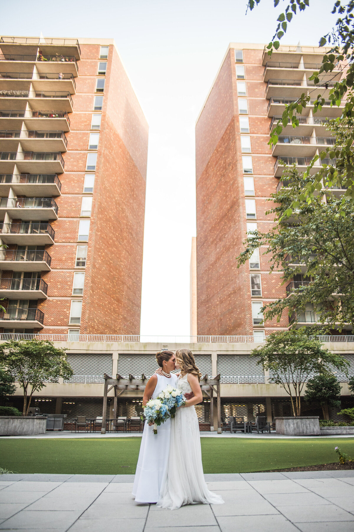 Two brides kissing in front of matching red brick buildings 