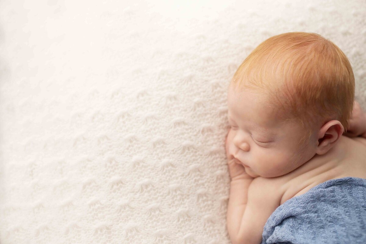 Adorable red-haired newborn boy in a relaxed pose on a neutral backdrop, highlighting his delicate features