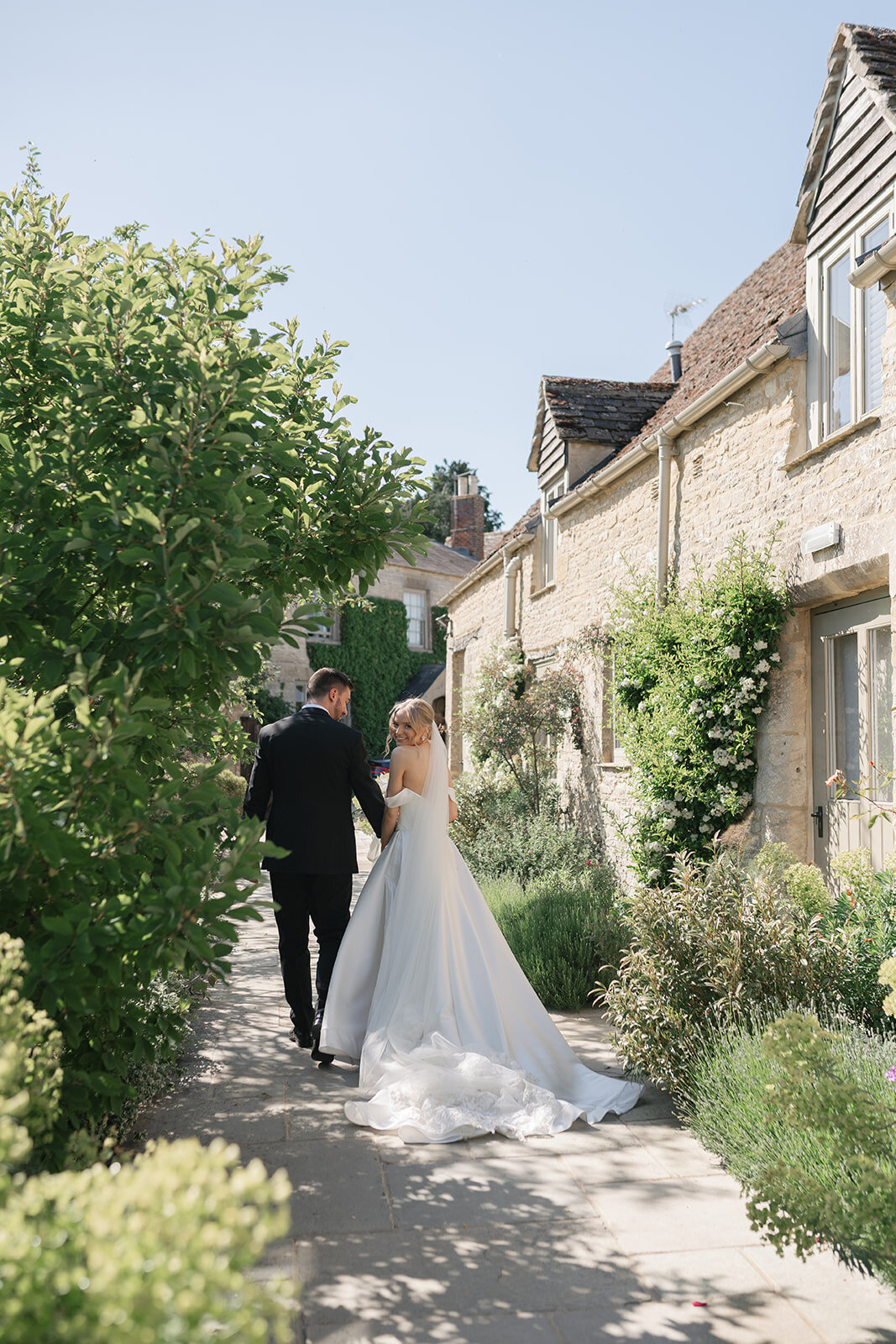Bride and groom walking along the path outside Caswell House on a sunny summer wedding day