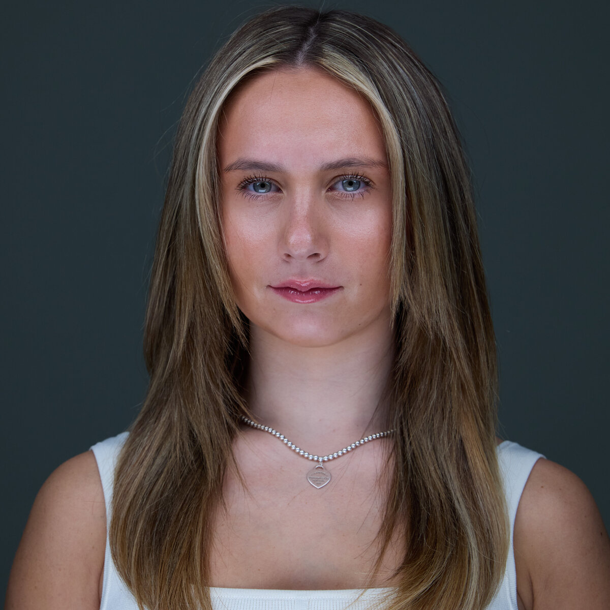 Headshot in CT of young woman with straight blonde hair, wearing white top, against gray backdrop by Rob Faber Photography.