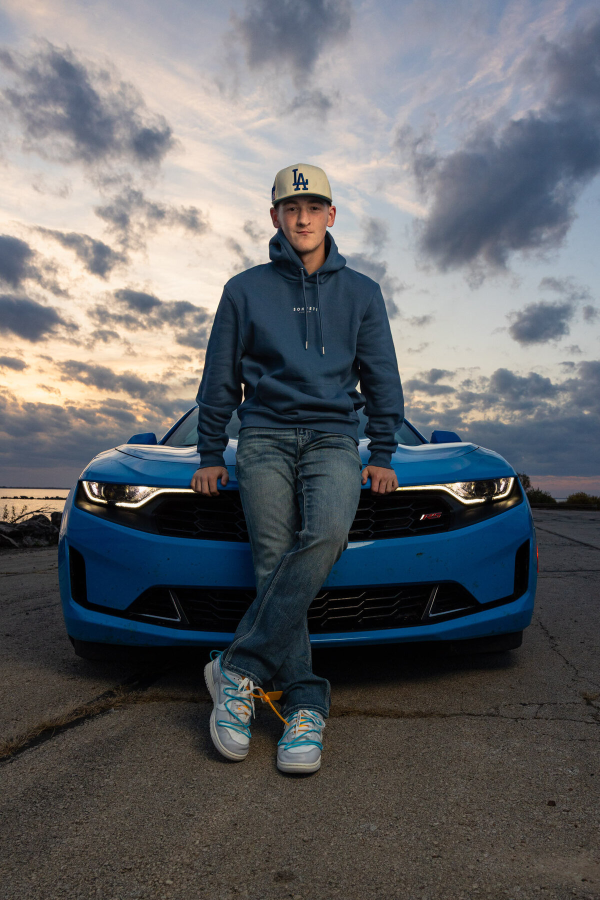 A senior guy sitting on the hood of his car at golden hour in Lawrence, KS