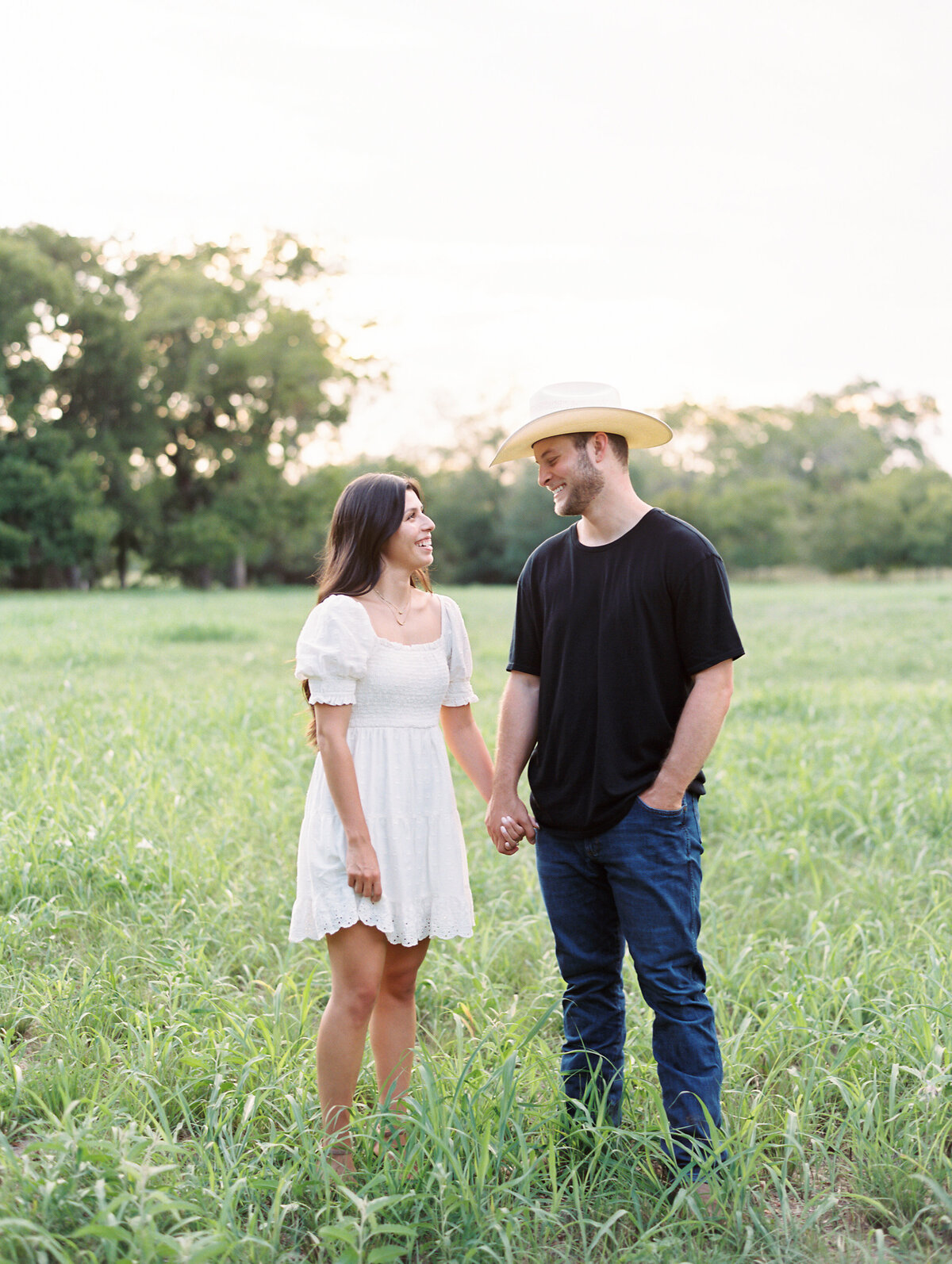 Woman in a white dress holding hands with a man in a black shirt and cowboy hat
