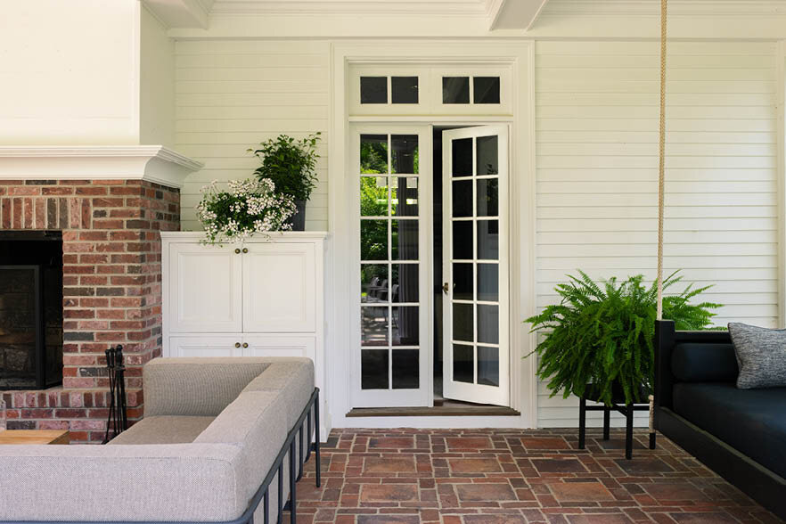 The covered patio features a cozy fireplace, cool sofas, and a low, wide teak coffee table from Design Within Reach, as seen on Boston Home Magazine's Instagram.