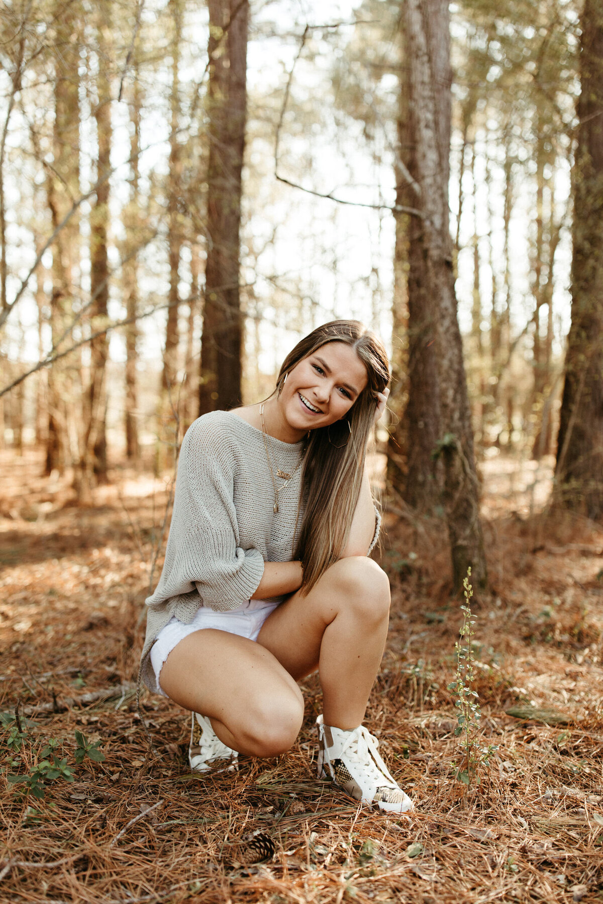 Girl senior squatting and posing in the woods during her outdoorsy session